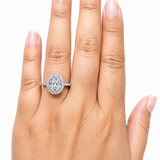 Hand displaying a 2.00 CTW DEW Oval Moissanite Halo Engagement Ring | GRA Certified 925 Silver on the ring finger, showcasing the oval-shaped stone surrounded by a halo of smaller stones on a silver band.